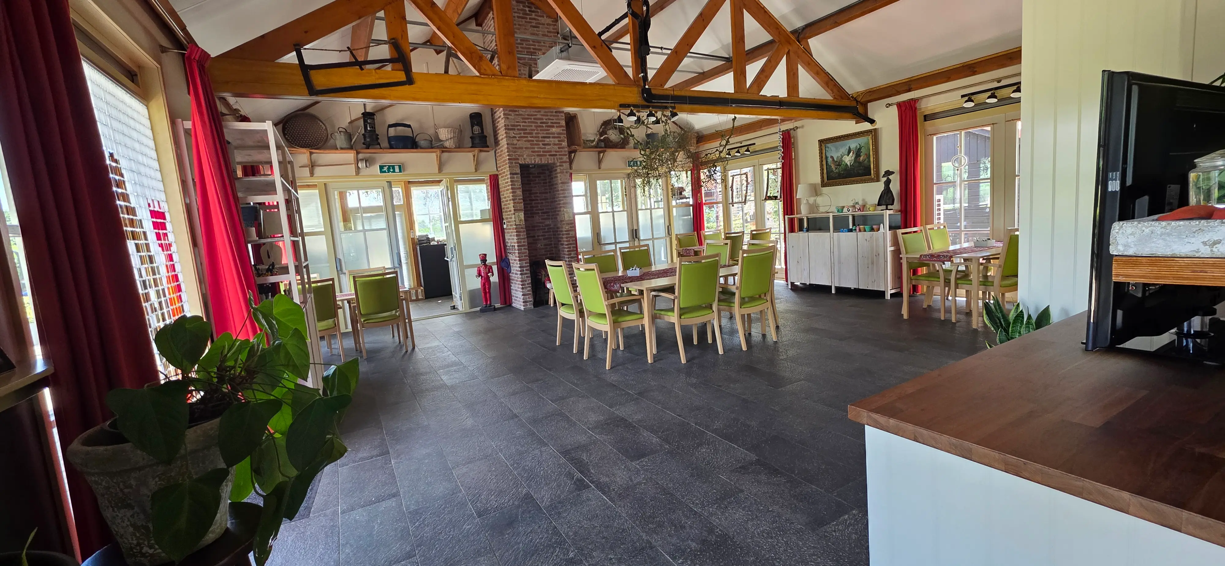 De lichte gemeenschappelijke ruimte van De Walkant met houten dakspanten, gedekte tafels en groene stoelen.