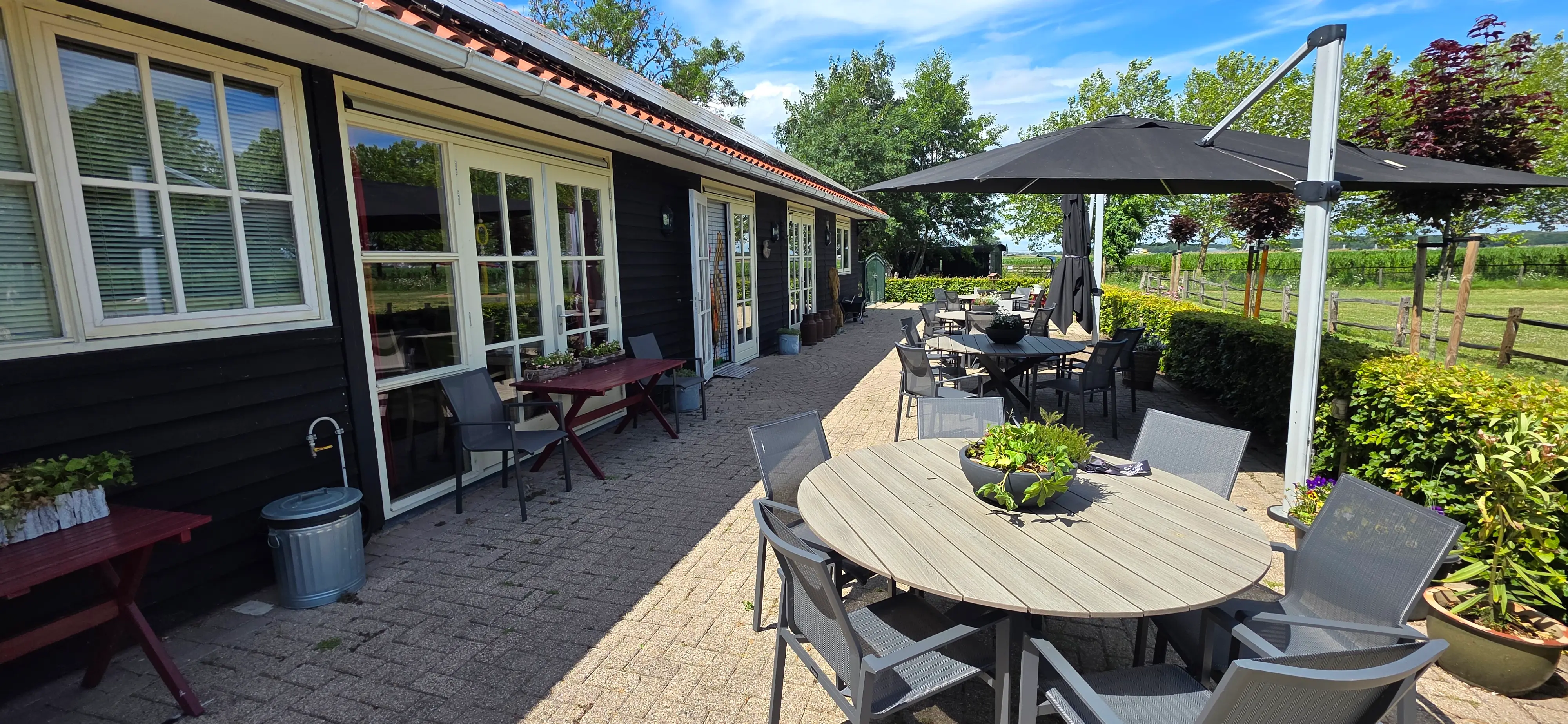 Het zonnige terras van De Walkant met tuintafels, stoelen en een parasol langs het gebouw.
