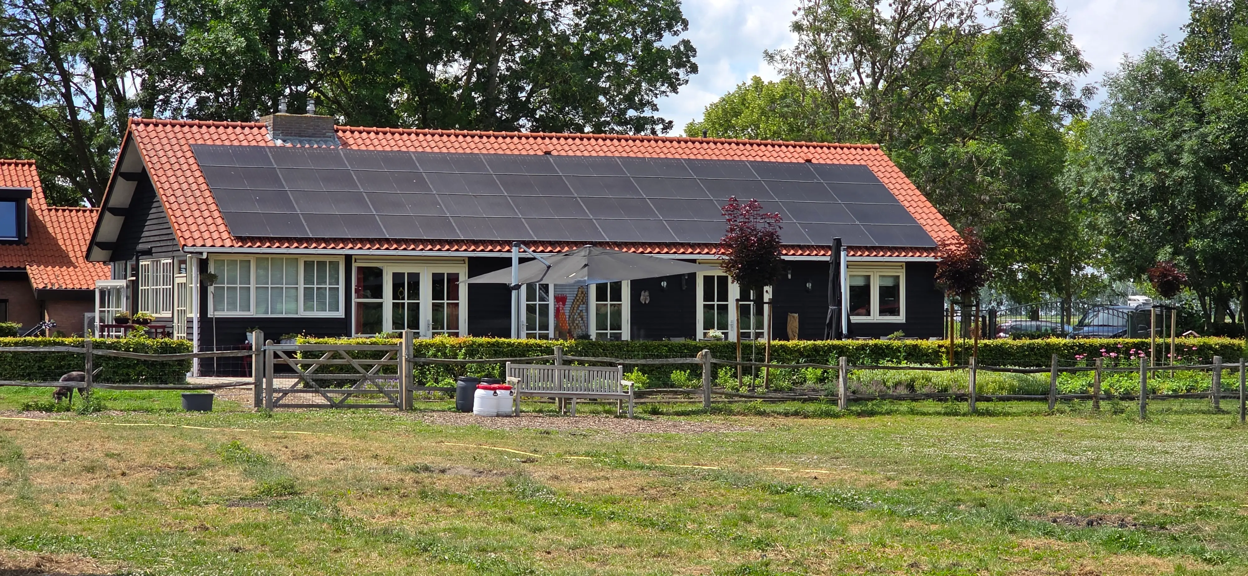 De Walkant gezien vanaf de wei: het gebouw met zonnepanelen op het dak, een tuinbank en een omheind weiland.